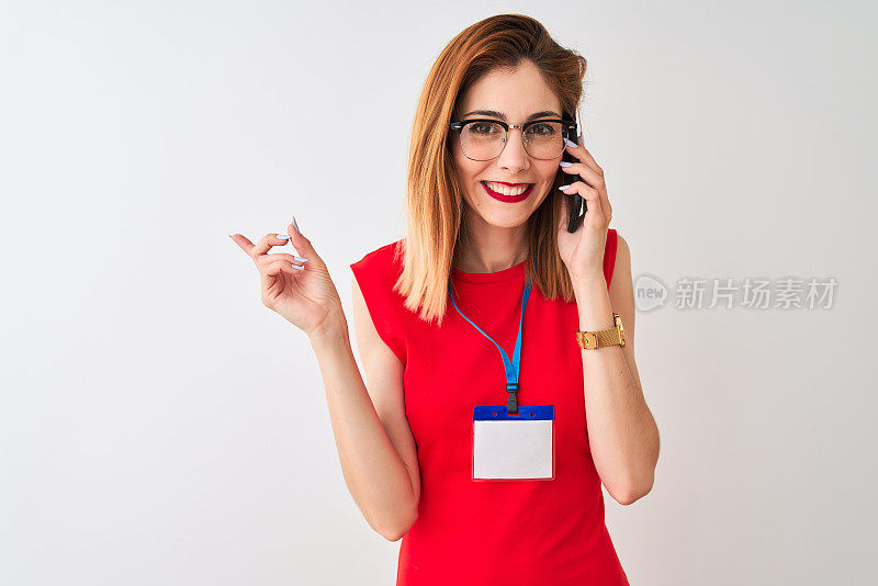 红发女商人戴着身份证，在孤立的白色背景下用智能手机聊天，非常高兴地用手和手指指着一边