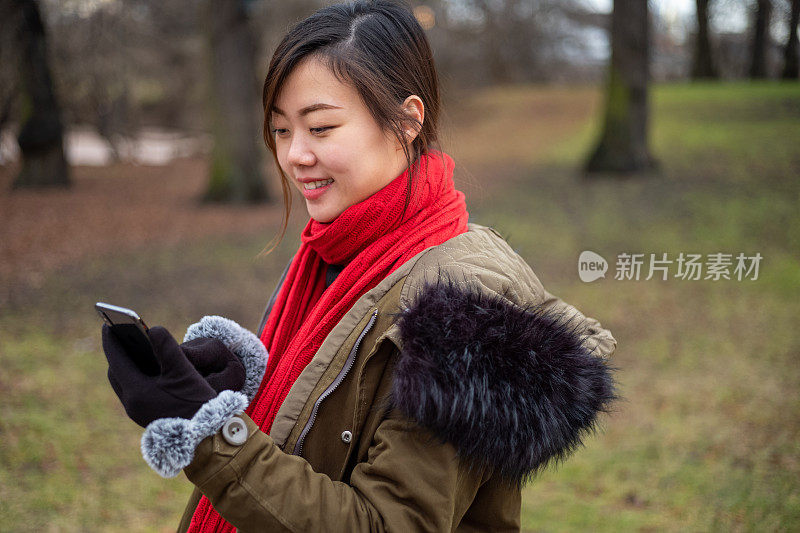 年轻的亚洲女性在温暖的冬天使用智能手机