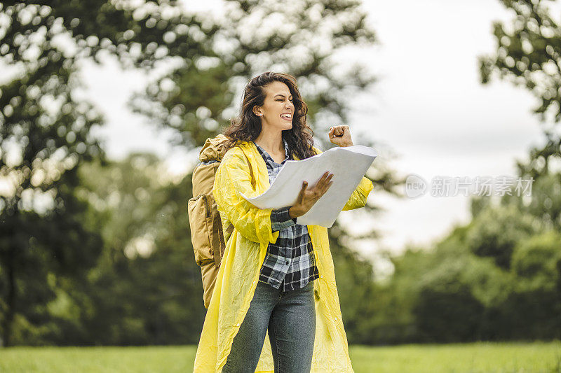 年轻女子穿着防水夹克，看地图，在雨中徒步旅行