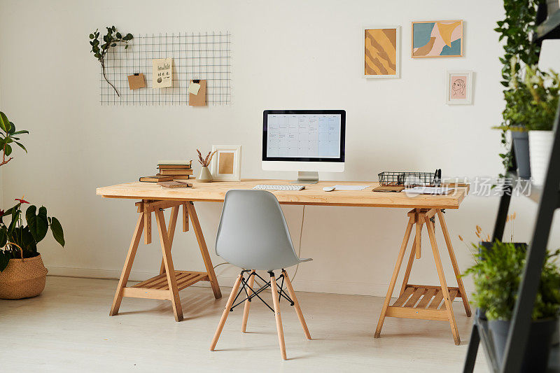 现代的家庭办公室，木制的桌子，电脑，规划板和抽象的图片在墙上