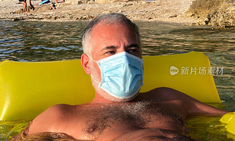 成年男子戴着防护面罩，躺在海上的充气泳池上