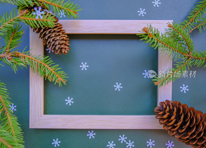 圣诞贺卡。木画框横跨冷杉树枝，球果，白色的金属箔。圣诞模型与冷杉树枝，球果在蓝色的背景。前视图。平的。副本的空间。
