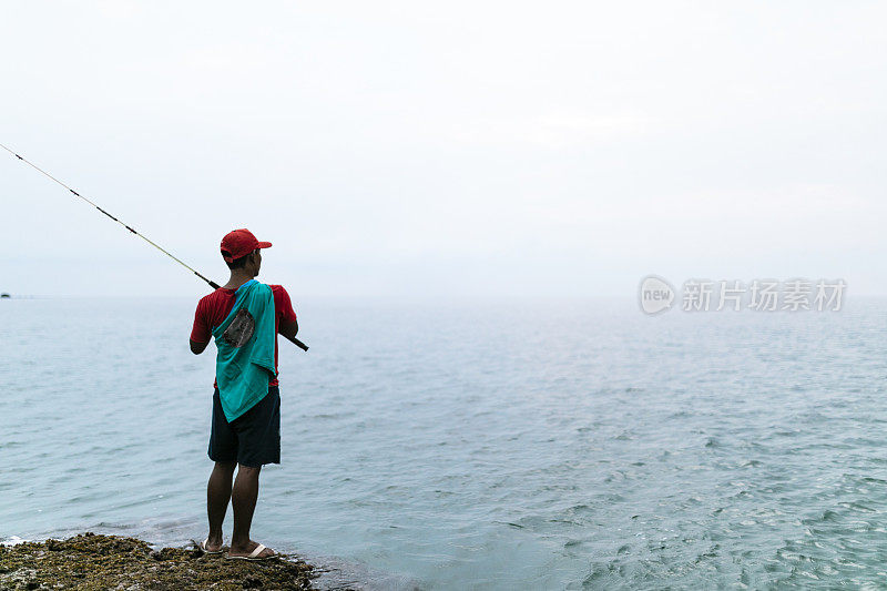 亚洲男子戴着帽子在海滩上钓鱼