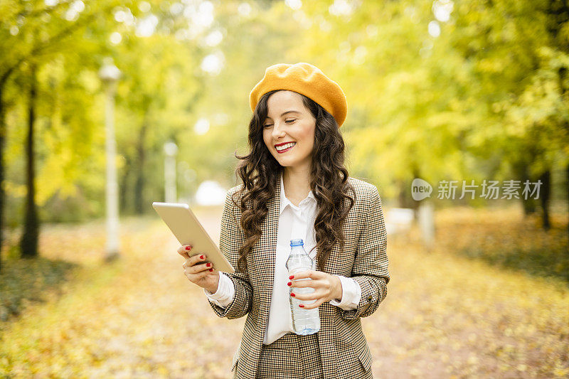 在她的数字平板电脑上喝水和阅读电子书的活力女人