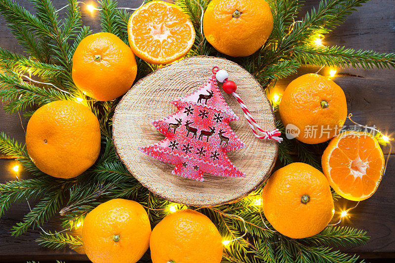 红色的圣诞树玩具树上的圆形切割周围的橘子，活冷杉树枝和金色的灯花环。柑橘的香气，一片片的橘子，圣诞的气息。框架，新年的背景
