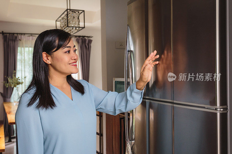 亚洲成熟女性在家中厨房使用智能冰箱或UX界面(空白智能冰箱)，智能未来家居和物联网概念