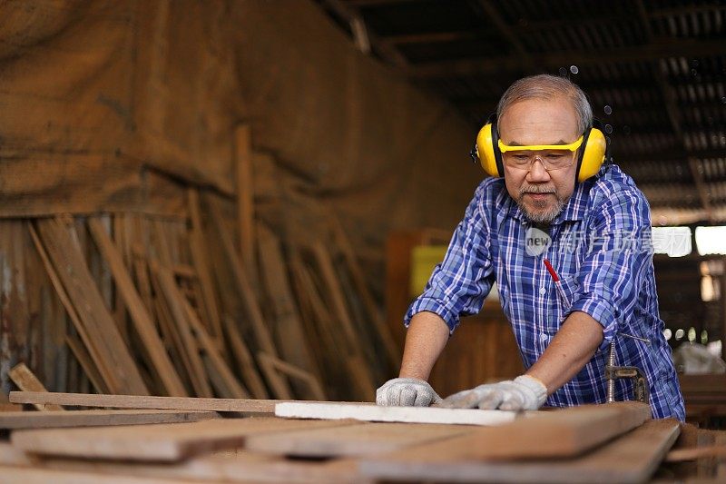 年长的亚洲木匠正在他自己的车库风格的车间里锯木板在退休年龄的爱好
