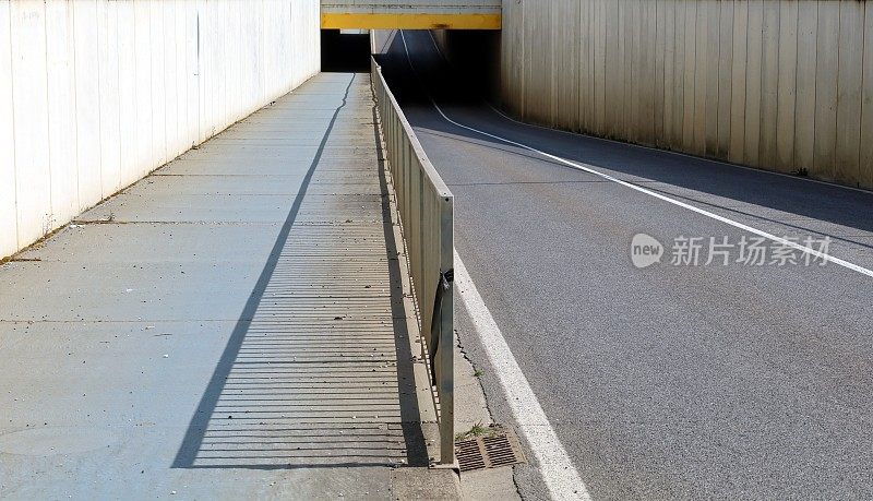 两条车道的道路，旁边有一条人行道和一条自行车道，中间有栏杆隔开。前面有一个地下通道，两侧有高高的混凝土墙。