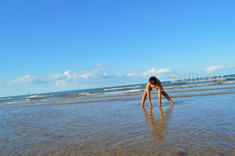 一个十岁的小男孩弯着腰在英国诺福克的海滩上摆姿势照相
