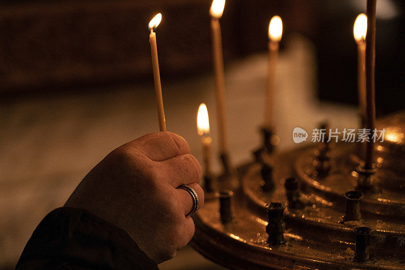 格鲁吉亚巴统——2021年3月15日:身着红色夹克的妇女的手点燃了教堂蜡烛