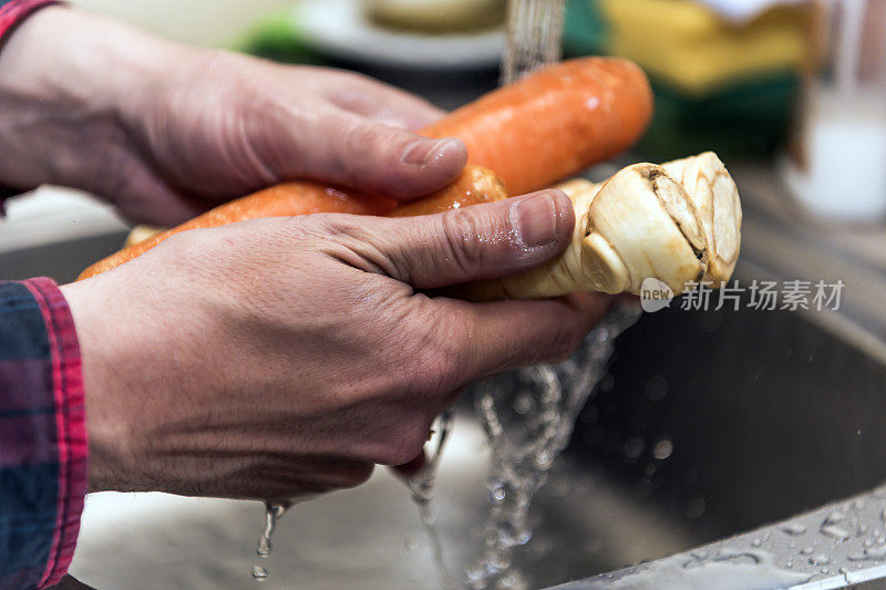 一个男人在水槽里彻底清洗胡萝卜和防风草的照片。