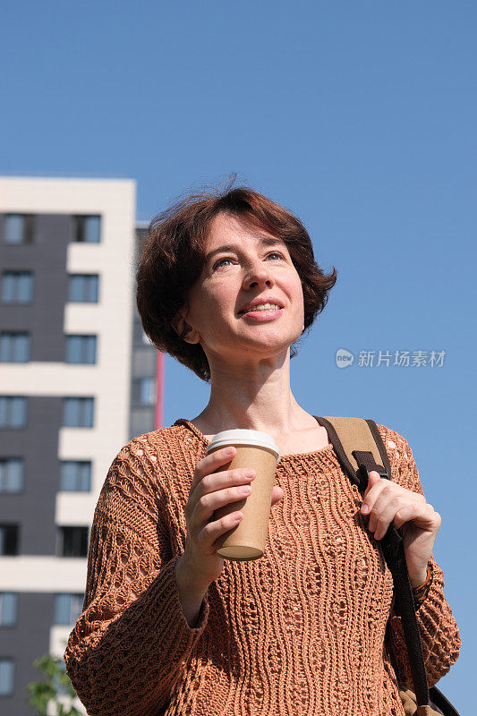 成熟的女人在城市的大街上等着用纸杯喝咖啡