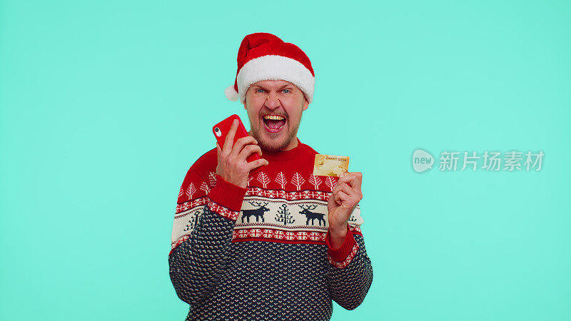 圣诞节穿红毛衣的男人用手机和塑料信用卡，赢了，庆祝，哇