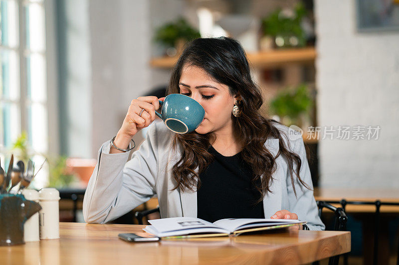 年轻的女商人在咖啡馆里看书喝咖啡。