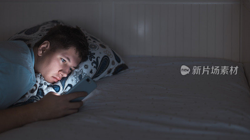 困倦的男人深夜在床上醒着，上网聊天。社交媒体成瘾，手机依赖，对眼睛的负面影响。