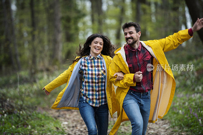 穿着雨衣的幸福情侣在大自然中牵着手旋转