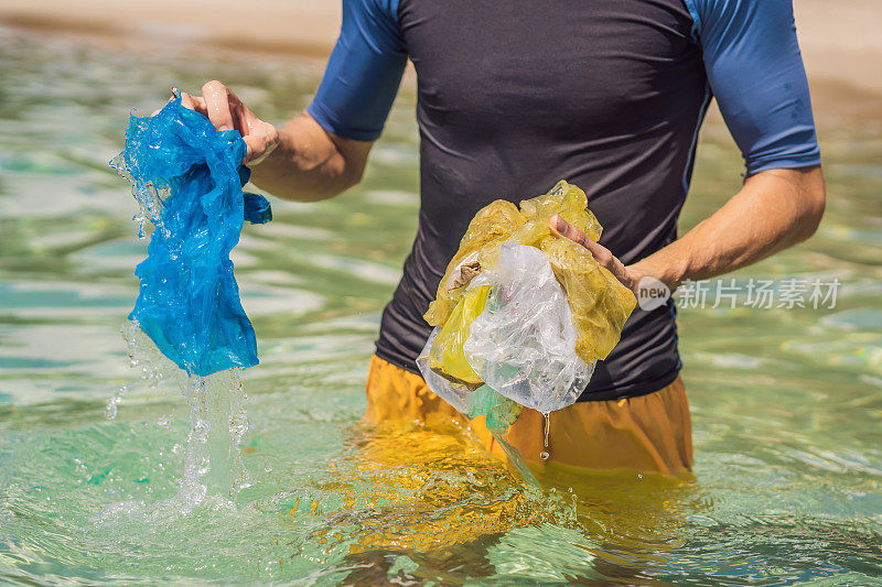 一名男子从美丽的蓝绿色大海中收集包裹。天堂海滩污染。沙滩上的垃圾垃圾洒在沙滩上造成的人为污染和环境问题，倡导志愿者概念清洁