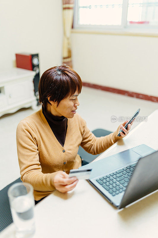 一位中年妇女正在家里用信用卡购物——技术与生活、信用卡、银行与支付的概念