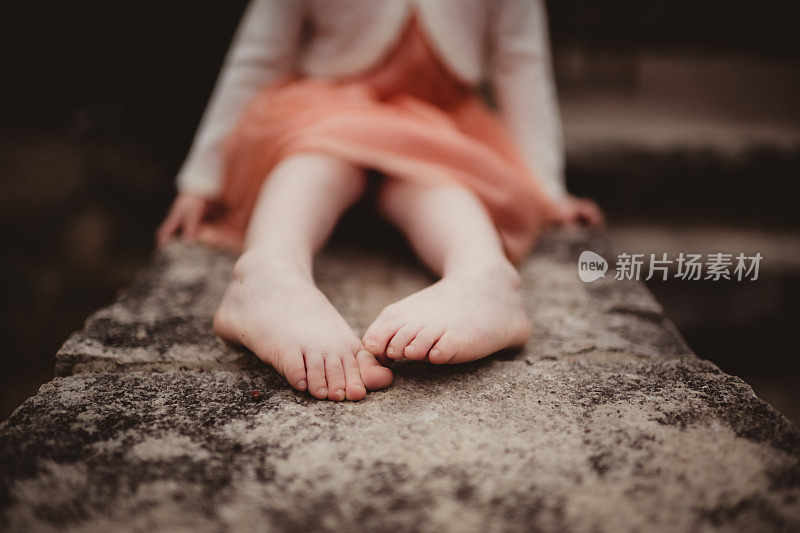 小女孩坐在一块石头上，脚趾头清晰可见