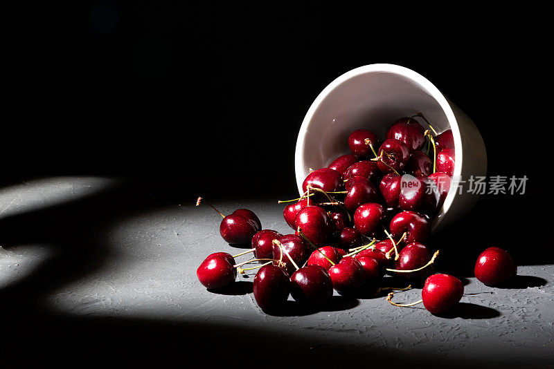 碗里盛满了深色背景的红樱桃。翻倒的杯子溢出了丰富而健康的樱桃