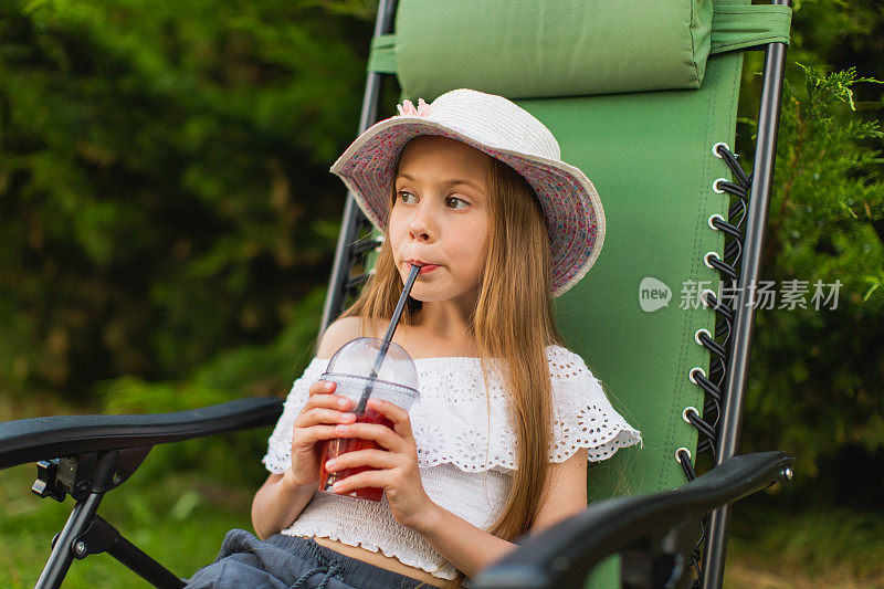 快乐的金发女孩穿着礼服，躺在后院的躺椅上。夏天的生活方式。的童年。