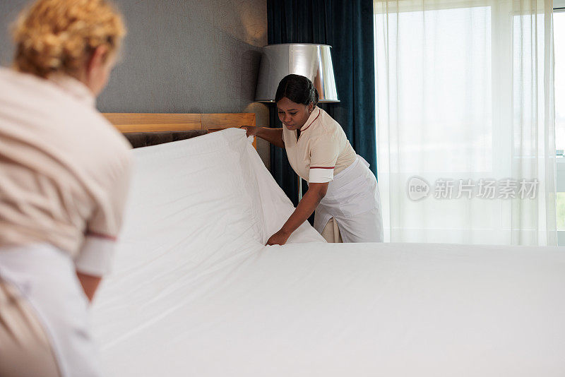 两个旅馆女佣把干净的床单叠在一起