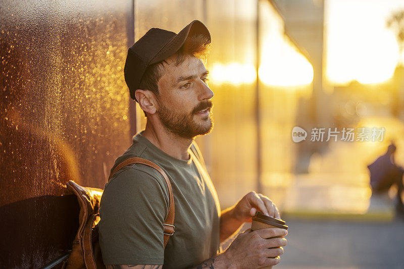 一个沉思的男人靠在街上的墙上，喝着一杯外卖咖啡休息一下。