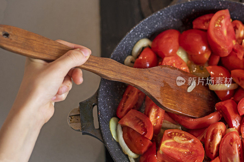 女孩用厨房里煎锅用的特制木铲搅拌西红柿和洋葱。flatlay