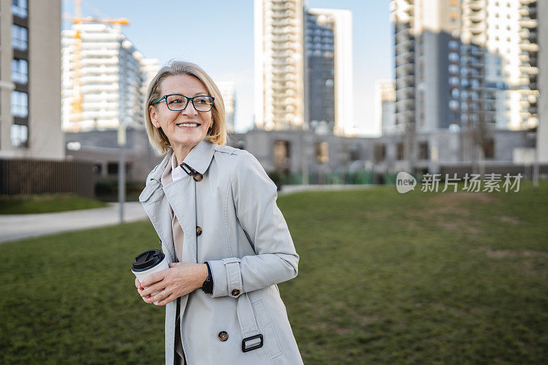 女人站在大楼前拿着咖啡去用手机