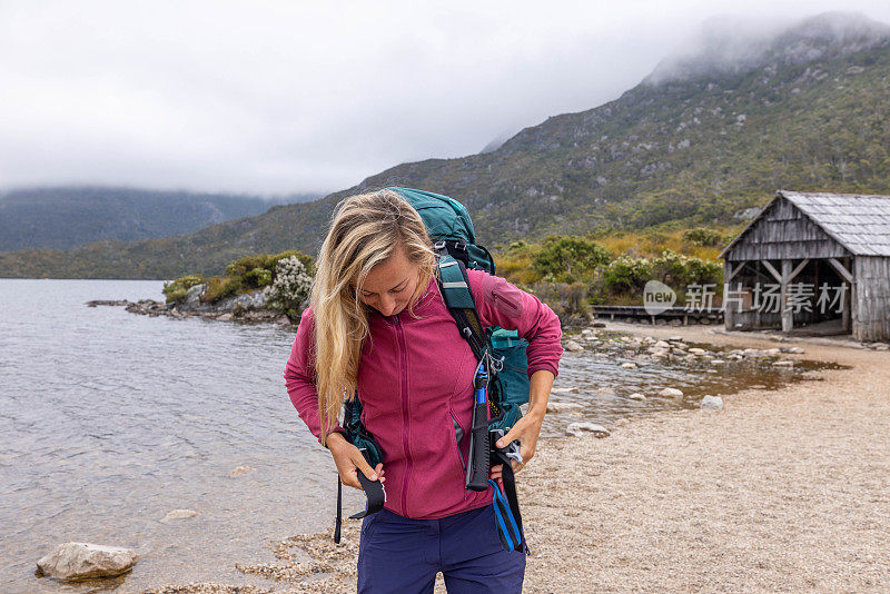 绿洲山:一个女徒步旅行者调整她的背包，暂停在雄伟的山峰湖