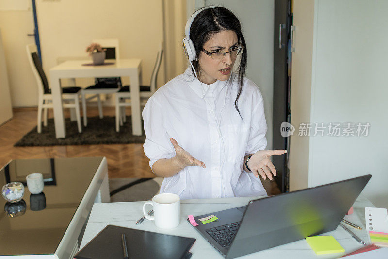 工作中的情绪。一位戴着耳机的沮丧的年轻女子正带着很大的压力在家办公室工作。现代虚拟理财顾问和咨询。远程办公，商务，自由职业者，网上购物，电子学习。