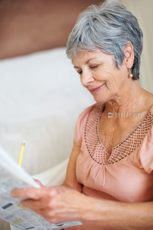 微笑的老妇人正在解报纸上的填字游戏