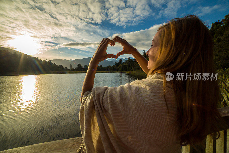 女人在山、湖、日出上做心形指架