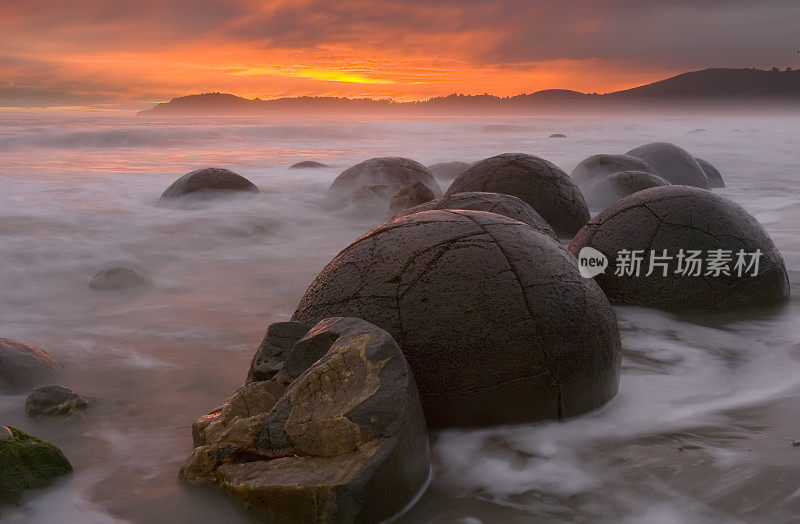 新西兰的莫拉基巨石在戏剧性的日出中冲浪