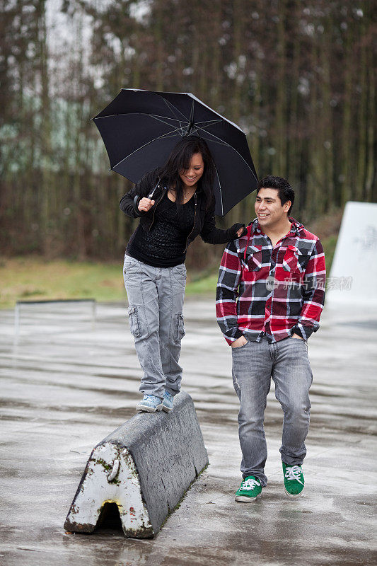年轻女子在外面用她的男朋友和雨伞保持平衡