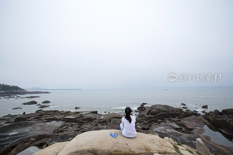 女孩坐在礁石上，面朝大海