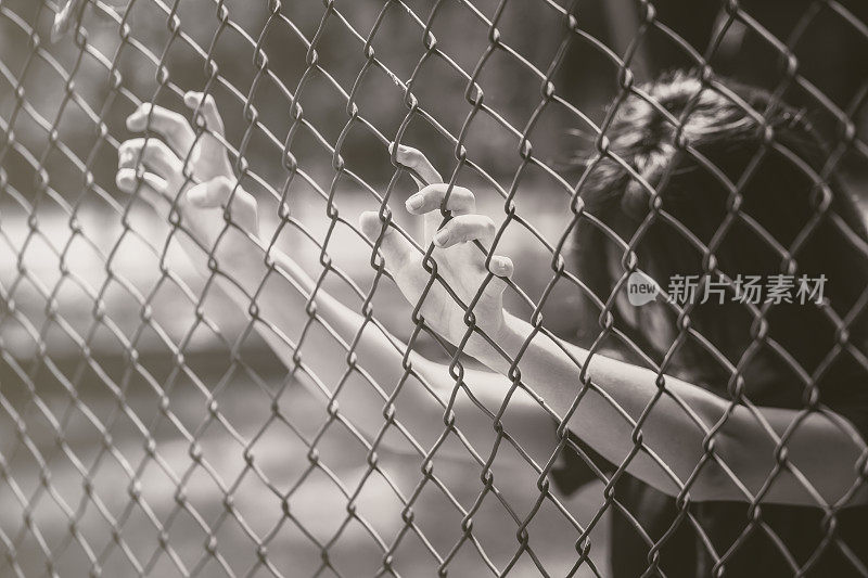少年背后的铁笼还是女子被囚，不快乐的少女手伤心绝望地在围栏监狱里蹲着，没有自由和自由奋斗的少年观念。