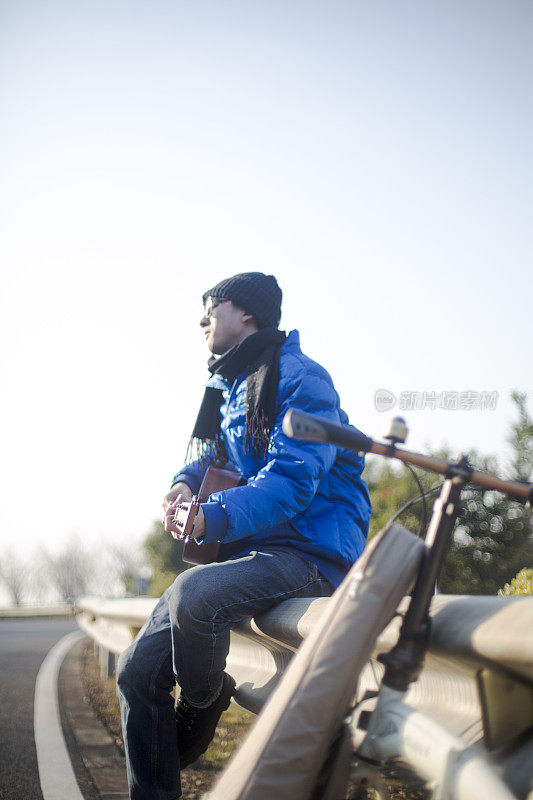 年轻的亚洲男子坐在公路栏杆上弹吉他