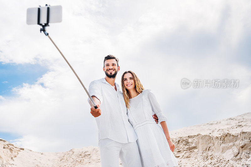 幸福的年轻夫妇用单脚架和智能手机在沙漠中自拍