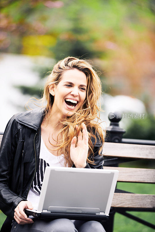 美丽的女孩坐在公园里，膝盖上放着笔记本电脑，玩得很开心，美国纽约联合广场