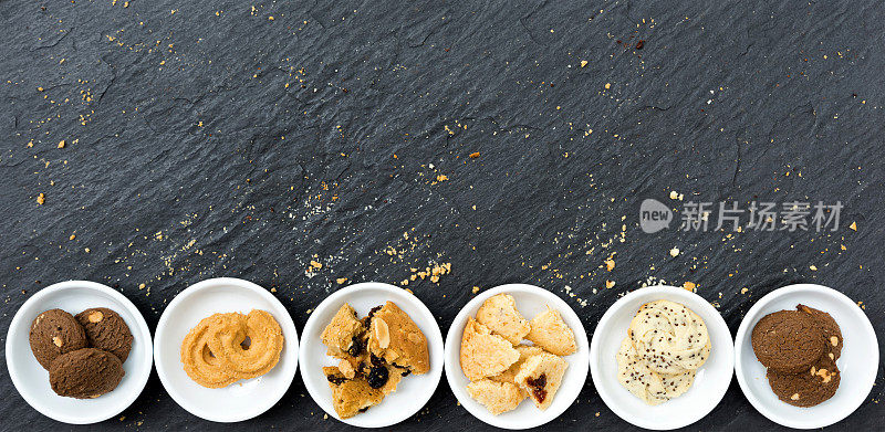 饼干和布朗尼饼干放在白色陶瓷容器中平铺在桌面上，顶视图不同的饼干在白色碗