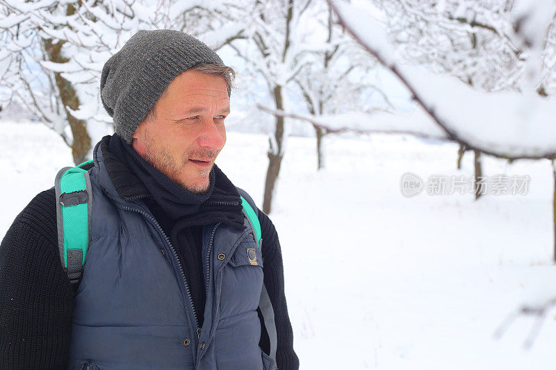 成年男子徒步旅行者戴着针织帽徒步在下雪的冬天的自然