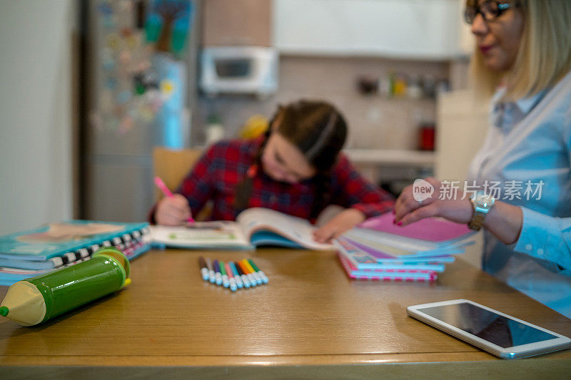 迷人的年轻女子和她可爱的小女儿正坐在桌旁一起做作业。母亲帮助女儿学习学校课程。