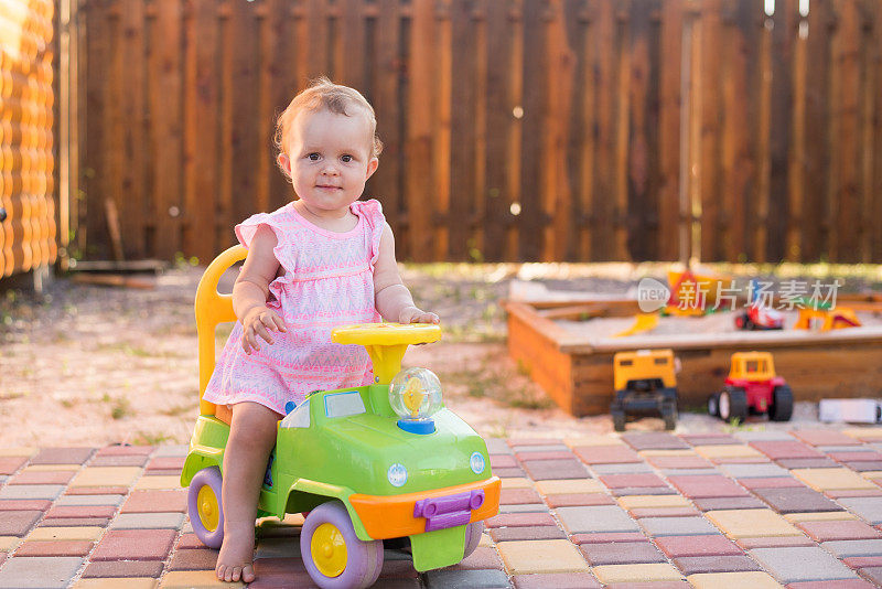 小女孩开着玩具车在户外的操场上，夏日背景，拷贝空间