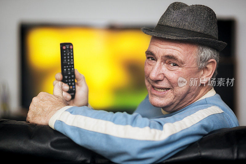 老人一边看电视一边拿着遥控器微笑