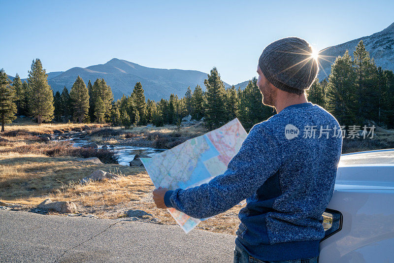 公路旅行概念;一名男子坐在汽车引擎盖上，在地图上查看方向