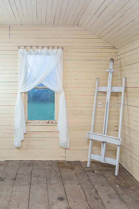 空白画布的画架，搭船的，在她的棚子里挂着窗帘的窗户旁边