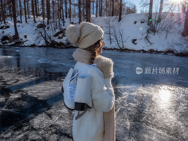 一个年轻女子肩上扛着冰鞋走在结冰的湖面上