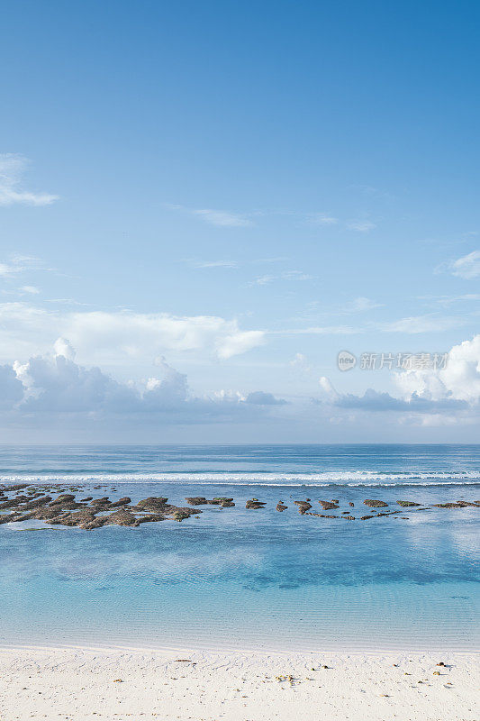 巴厘岛海滩的场景-蓝绿色的印度洋，白色的沙滩和蓝色的多云的天空在背景