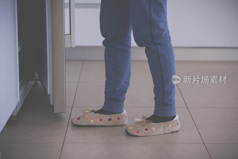 靠近女性的脚与拖鞋走在瓷砖地板上的厨房。打开冰箱的女人。